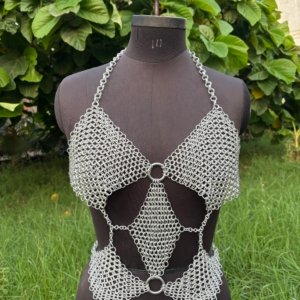 Geometric chainmail top for women on dress form, handmade silver metal crop top with cutouts and O-ring accents, outdoor setting.