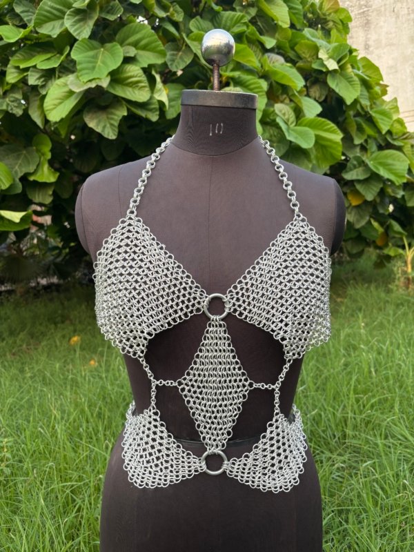 Geometric chainmail top for women on dress form, handmade silver metal crop top with cutouts and O-ring accents, outdoor setting.