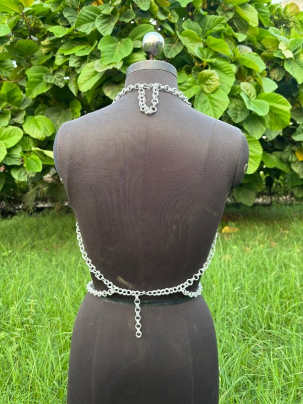 Geometric chainmail top for women on dress form, handmade silver metal crop top with cutouts and O-ring accents, outdoor setting.