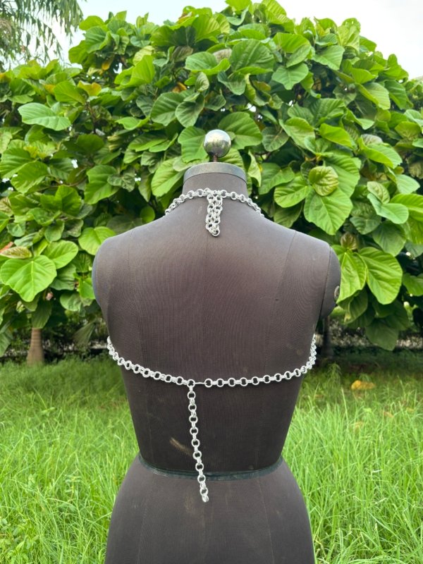 Chainmail halter top for women displayed on a dress form, handmade metal fashion armor top with draped chains, outdoor photo.