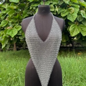 A handmade chainmail halter top displayed on a black dress form, featuring a deep V-neckline and pointed hem design. The top is crafted from interlinked metal rings in a dense weave, creating a medieval-inspired yet modern fashion piece.
