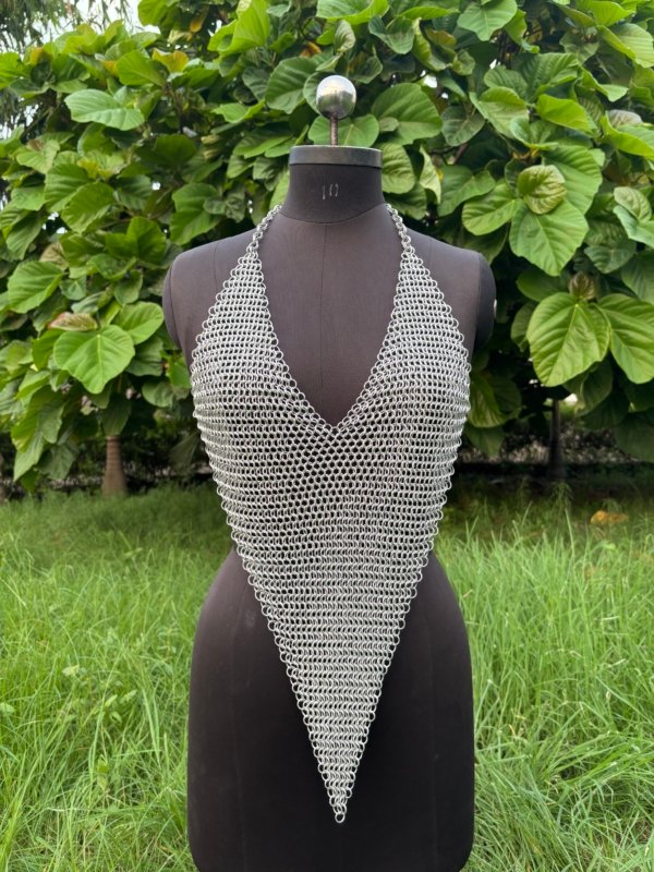 A handmade chainmail halter top displayed on a black dress form, featuring a deep V-neckline and pointed hem design. The top is crafted from interlinked metal rings in a dense weave, creating a medieval-inspired yet modern fashion piece.