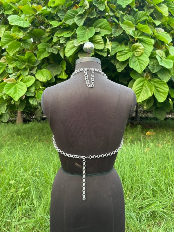 A handmade chainmail halter top displayed on a black dress form, featuring a deep V-neckline and pointed hem design. The top is crafted from interlinked metal rings in a dense weave, creating a medieval-inspired yet modern fashion piece.